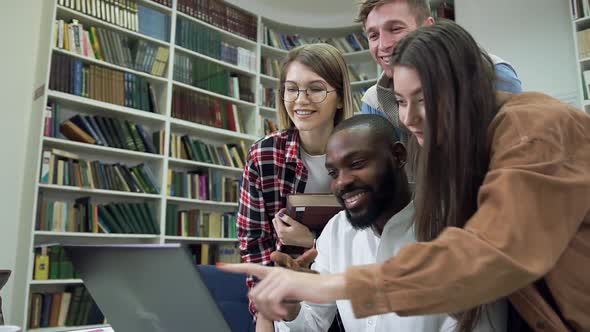 Modern Multiethnic Friends Working Over Home Task in the Library Using Computer alt