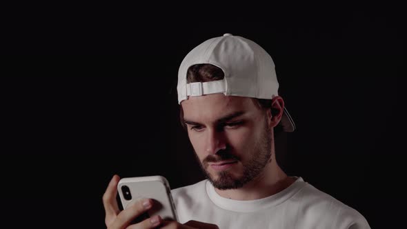 Trendy 20s Man using and typing on phone, close, black background