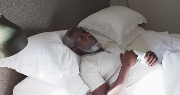 Sick senior african american man couching while lying on the bed at home