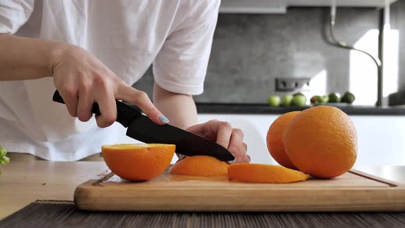 Girl Cutting Orange Into Slices on a Bamboo Board in Kitchen