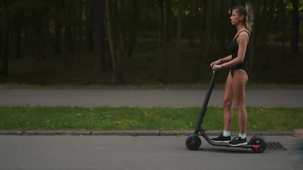 Follow Shot Confident Slim Woman is Riding Her Electric Scooter Around an Evening Park