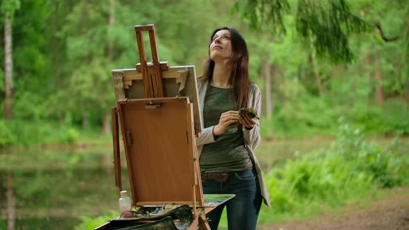 Middle View of a Beautiful Brunette Woman Painting a Picture on Canvas in a Park