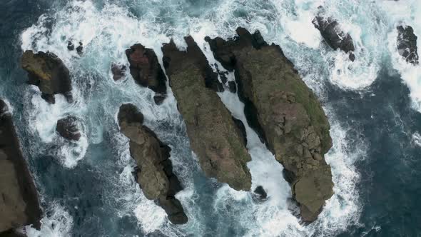 Aerial view of the crispy waves breaking on the rocks.