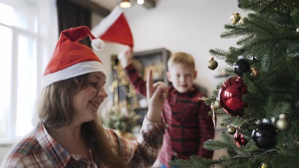 Caucasian Mom and Son in Santa Hats Having Fun Decorate the Christmas Tree