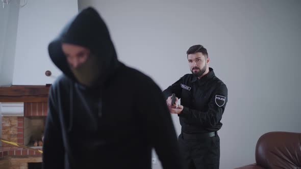 Confident Caucasian Police Officer Raising Up Gun and Shouting at Criminal, Man in Black Mask