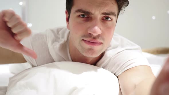 Thumbs Down By Man Lying in Bed on Stomach Disliking