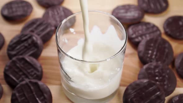 A glass of fresh yogurt on a wooden table with chocolate cookies. Pouring thick kefir in slow motion