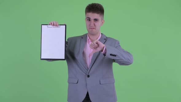 Serious Young Businessman Showing Clipboard and Giving Thumbs Down