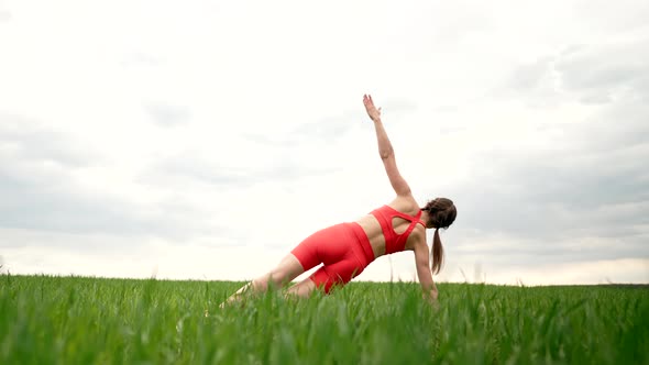 Strong Woman in Orange Wear Doing Yoga Vasishthasana Side Plank in Green Field