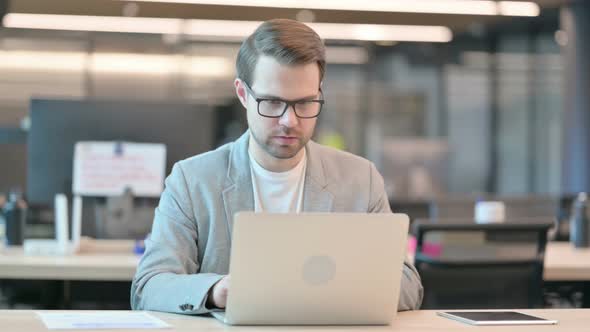 Man Looking at Camera while using Laptop in Office