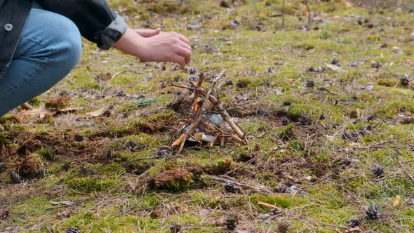 Young Male Making a Small Forest Campfire Using Sticks and Warming Up His Hands