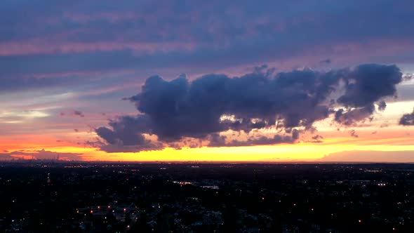 An aerial timelapse of the colorful sky as the sun sets. There are dark clouds rolling towards the d