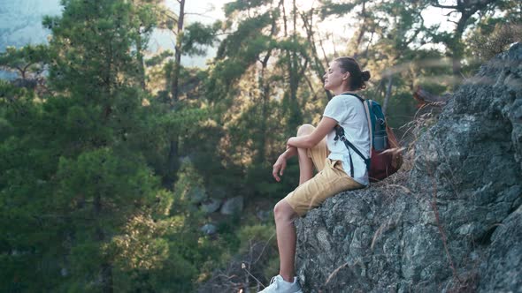 Young Woman with a Backpack Sitting on a Rocky Mountain and Enjoying Fresh Air