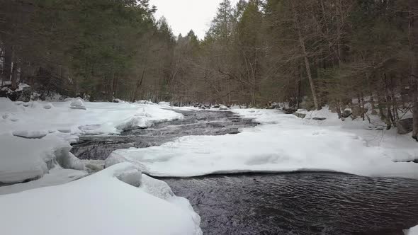 Drone shot flying low above snowy river rapids in winter