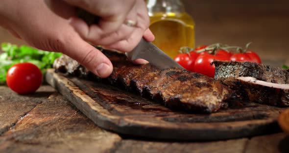 Men's Hands with a Knife Cut the Ribs of Grill To Pieces. 