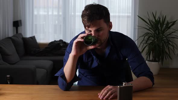 Medium shot of a young hangover man drinking beer at home in modern apartment.