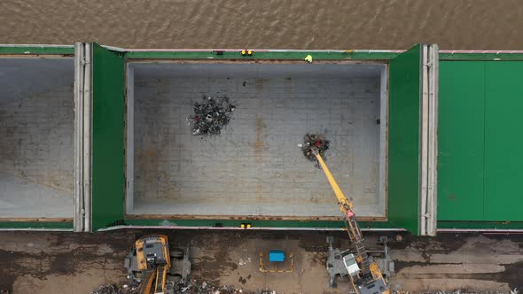 Aerial birdseye footage of mechanical grab machines loading scrap metal onto a ship.