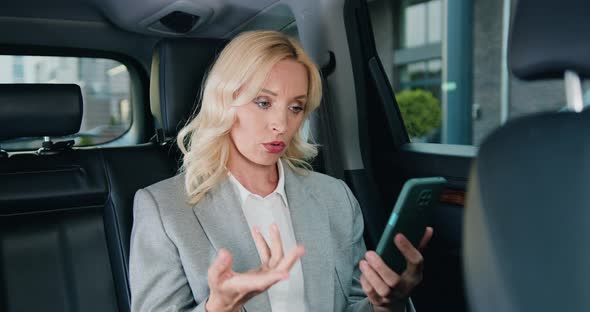 Serious Caucasian Business Lady Talking on Smartphone in Modern Car.