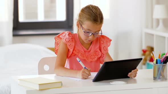 Girl with Tablet Pc Writing To Notebook at Home