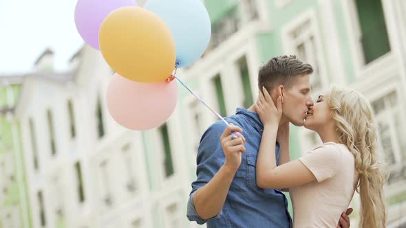 Couple walking down street, stopping to kiss, guy holding balloons, feelings