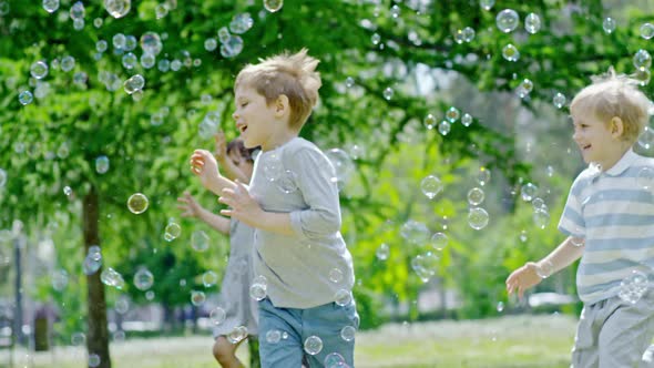 Excited Children Running through Lots of Soap Bubbles in Park alt