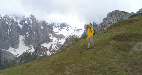 Hiker Goes on a Hill Against the Background of Snow-capped Mountains