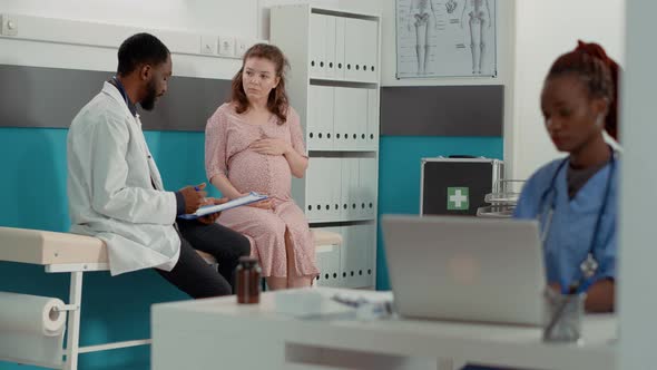 African American Doctor Consulting Pregnant Woman on Bed