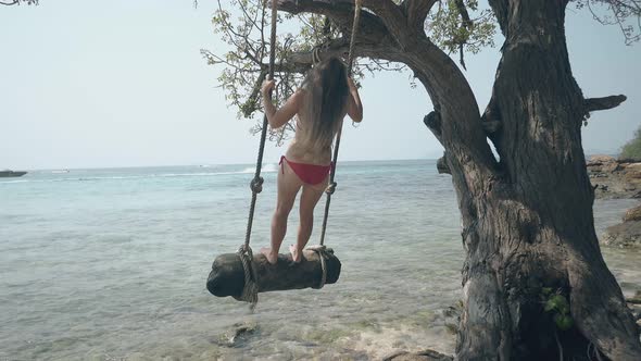 Tourist Swings on Log Hung on Tree at Calm Ocean Beach