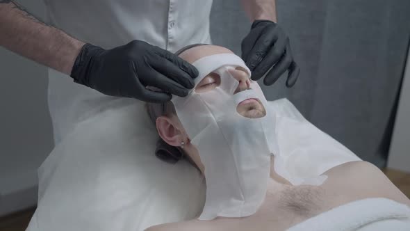 Male Hands Taking Off Cotton Facial Mask From Face of Young Bearded Handsome Man Lying with Closed