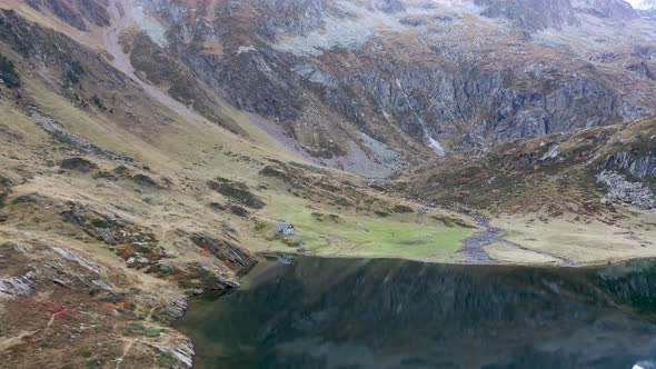 Small cabin at the edge of Lac d'Espingo lake in Haute-Garonne, Pyrénées, France, Aerial approach sh