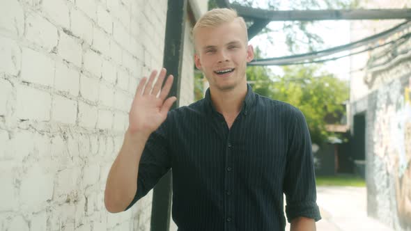 Slow Motion Portrait of Handsome Young Man Waving Hand and Smiling Standing Outside in City Street
