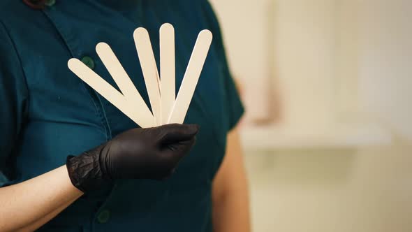 Female Hands in Black Gloves Holding Set of Spatulae for Waxing or Sugaring