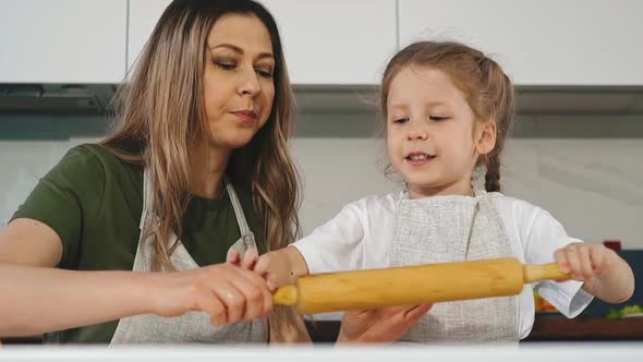 Mother Gives Little Girl Wooden Pin To Roll Dough at Table