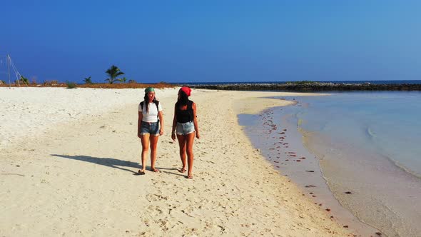 Pretty smiling ladies on vacation spending quality time at the beach on paradise white sand and blue