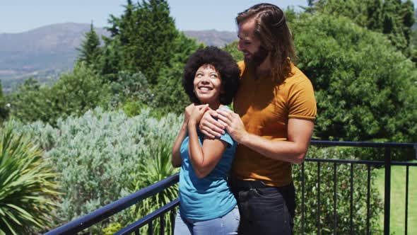 Mixed race couple embracing each other and enjoying the view while standing in the balcony at home