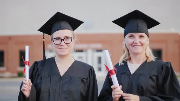 Two Female College Graduate Students in Gowns and Graduation Caps in Front of a College Building