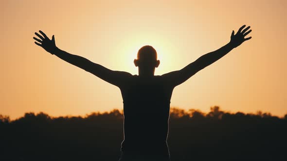 Silhouette of Young Man Raising Hands To Sides and Up Against Sunset Slow Motion