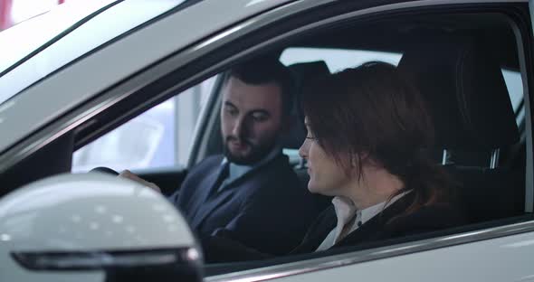 Adult Caucasian Woman and Young Man Sitting in Car and Talking. Female Client and Male Trader