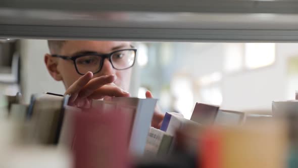 Man Looking For Book On Bookshelves At Library At College