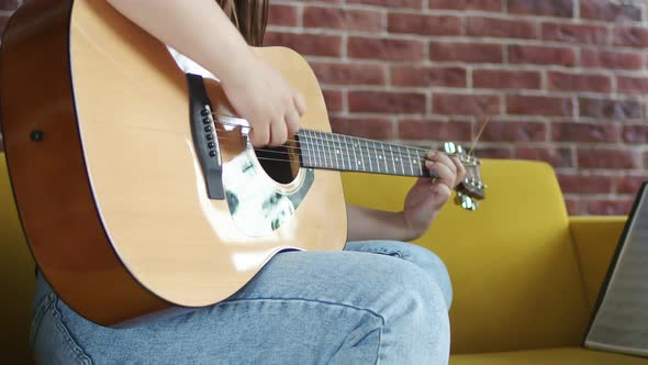 Woman is Sitting on Sofa and Playing an Acoustic Guitar Strumming Strings