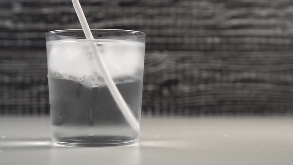 A bartender hand stirs a drinking tube with ice cubes in a glass cup