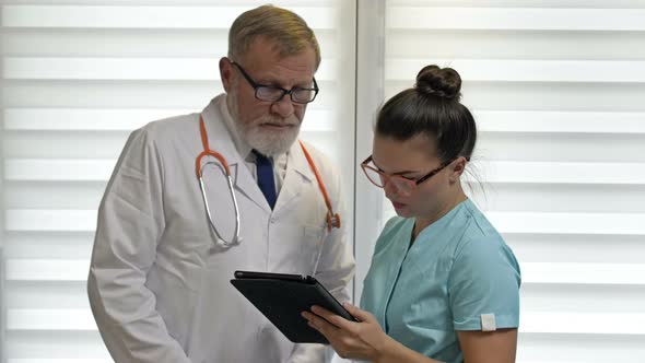 An Elderly Experienced Doctor Gives Instructions To a Young Nurse.