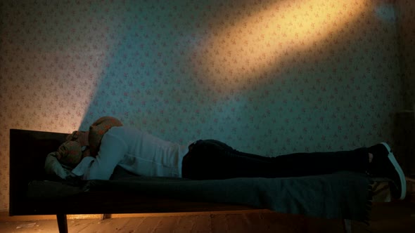 A man lies on the bed of an old apartment and covers his head with a pillow	