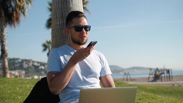 Handsome Man Sitting on the Grass in the City with a Laptop and Talking on the Phone Job Search Rest