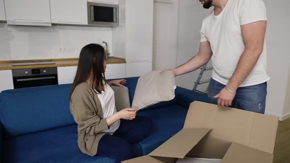 Married Couple with Pregnant Wife in the Living Room Unpacking Pillow From the Box