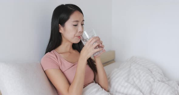 Woman drinking glass of water on bed 