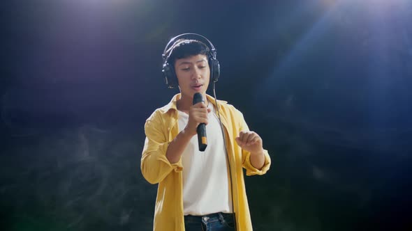 Young Asian Boy With Headphone Holding A Microphone And Singing On The White Smoke Black Background