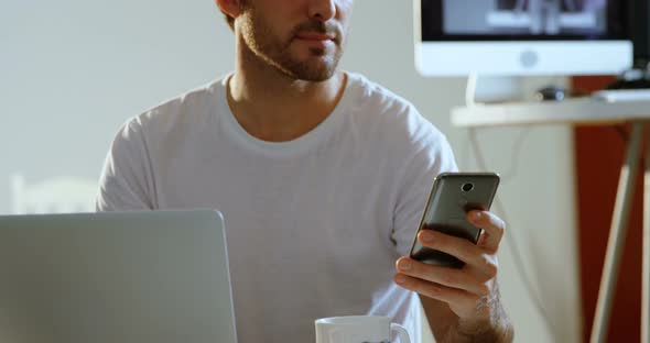 Male photographer using mobile phone while working on laptop