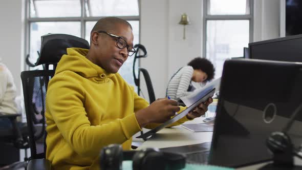 Portrait of smiling african american creative businessman sitting by desk in modern office