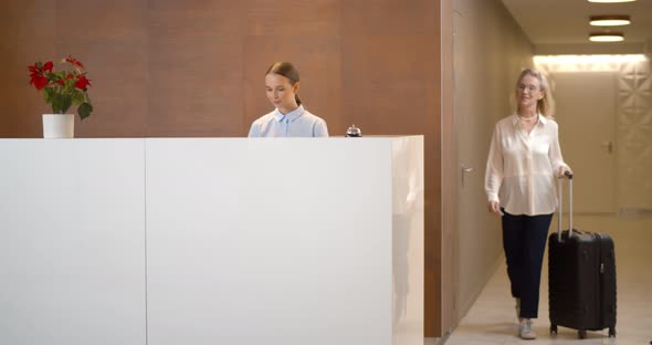 Elegant Mature Woman with Suitcase Checking Out Hotel Leaving Key Card at Reception Desk